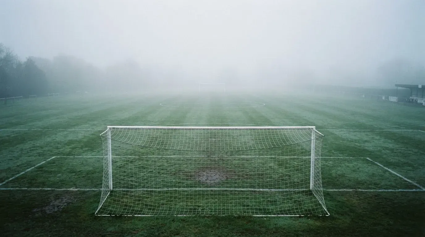 Ein leeres Fußballfeld im Morgennebel, die Mittellinie verliert sich im Dunst, kein Mensch ist zu sehen.