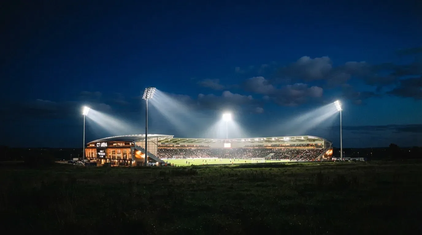 Ein Stadion unter Flutlicht aus großer Entfernung gesehen, der Himmel darüber ist tiefblau.