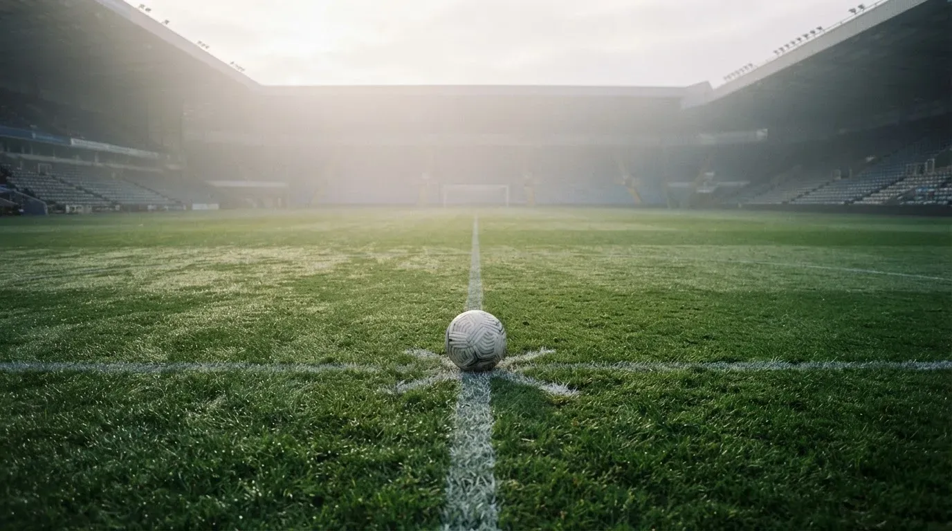 Ein Fußball liegt auf dem Anstoßpunkt eines leeren Rasenplatzes im Morgennebel.