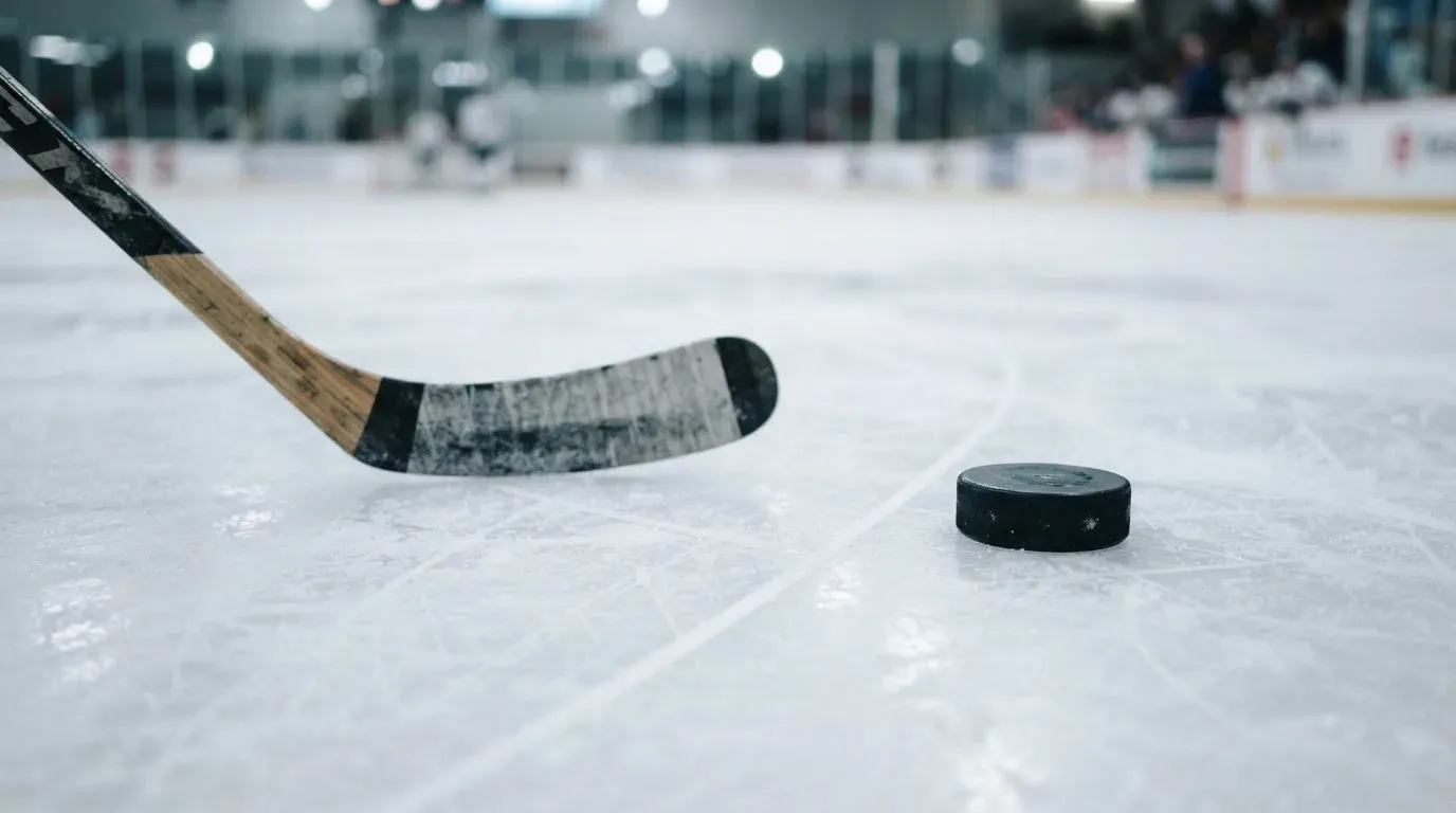 Ein Eishockeyschläger und ein schwarzer Puck liegen auf dem Eis, eine Kratzspur zieht sich durch das Bild.