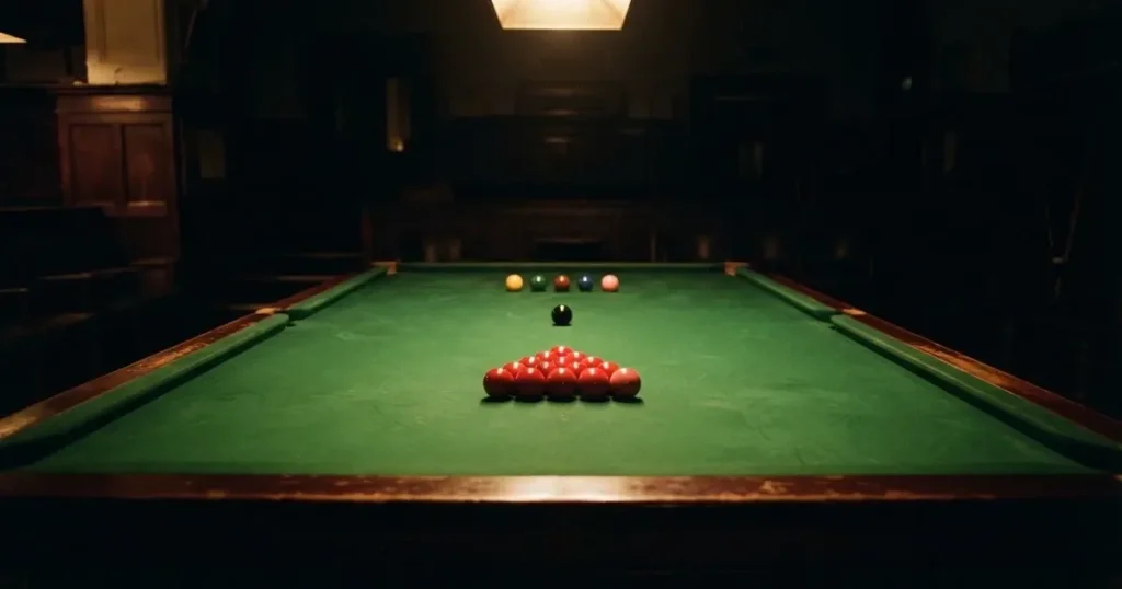 Ein Snookertisch mit grünem Tuch in einem abgedunkelten Saal, ein Lichtkegel fällt von oben auf die aufgestellten Kugeln.